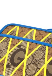 Sac en tissu marron et beige à motif avec logo "GG" répété, accentué par des rayures diagonales jaunes vives et une bordure bleue.