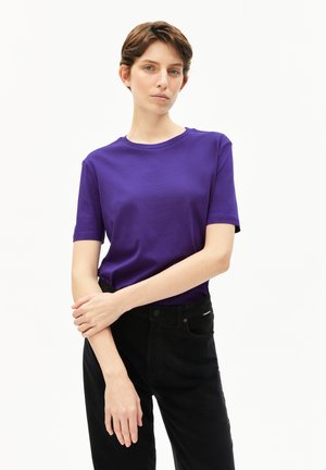 T-shirt en coton violet à manches courtes, col rond et texture lisse, associé à un pantalon noir taille haute avec une fermeture à bouton.