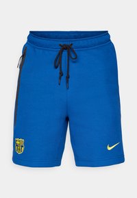 Calções de desporto azuis com painéis laterais pretos, cordão ajustável, logótipo do FCB em amarelo e Swoosh da Nike amarelo na parte inferior da perna direita.
