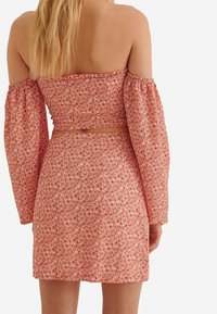 Mujer con un top de flores rojas sin hombros y una falda de talle alto a juego, vista desde atrás sobre un fondo blanco.