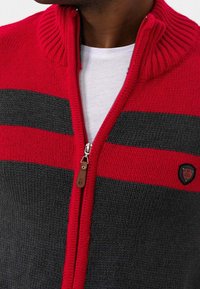 Rood en grijs gestreepte gebreide cardigan met ribbelkraag, ritsluiting en leren accent. Heeft een geborduurd logo aan de linkerkant.