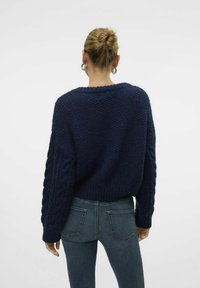 Navy blue knitted sweater with chunky cable-knit sleeves, cropped design, and textured fabric. Paired with fitted denim jeans.