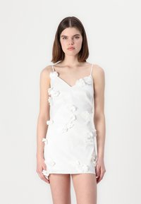 Vestido blanco con escote en V y tirantes finos, con aplicaciones florales tridimensionales dispersas, tejido suave y silueta ajustada.