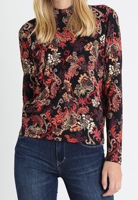 Top lungo nero a maniche lunghe con motivo floreale in rosso, arancione e crema. Tessuto morbido, scollo alto e design aderente abbinato a jeans scuri.