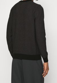 Maglione nero con texture e un motivo a griglia attillato. Presenta un colletto e polsini a coste, e un orlo nero solido.