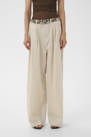 Beige hørbukser med vide ben og forreste plisseringer, kombineret med en brun rynket top og et bælte med slangeprint, båret med sandaletter med åben tå.