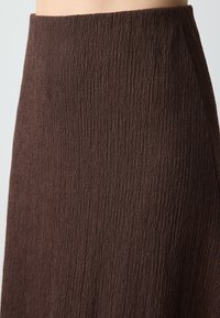 Jupe brune texturée avec un design froissé et une taille élastique. Le tissu présente une texture ondulée et côtelée sur toute sa surface.