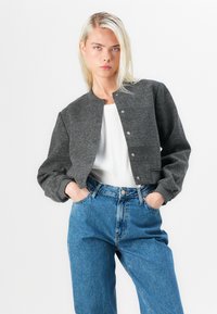 Gray cropped jacket with a round neckline and snap-button closure, paired with high-waisted blue jeans. Soft texture, relaxed fit.