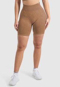Pantaloni corti marroni a vita alta realizzati in un tessuto morbido con un leggero lucido, caratterizzati da motivi testurizzati e una cintura liscia. Indossati con sneakers bianche.