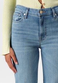 Jeans in denim azzurro chiaro con vita alta, cinque tasche, dettagli di cucitura discreti e chiusura con bottone frontale. Tessuto morbido e texture.