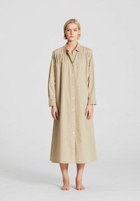 Robe chemise beige à manches longues avec un double boutonnage et un détail froncé aux épaules. Fabriquée en tissu léger, atteignant la mi-mollet.