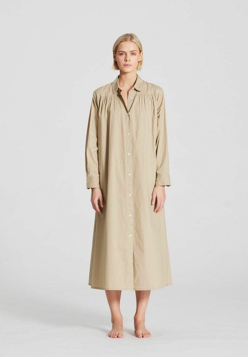 Beige, langärmad klänning med knäppning framtill och skrynkliga axeldetaljer. Tillverkad av lätt tyg och når mitt på vaden.