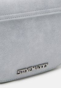 Grijze faux suede handtas met een gladde textuur, voorzien van een geperst merkembleem en stikdetails langs de randen.