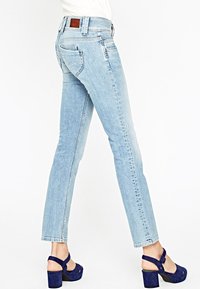 Ljusblå denimjeans med rak passform, ljus blekning och bakfickor. Matchas med marinblå högklackade sandaler.