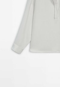 Maglietta a maniche lunghe grigio chiaro con collo a placket, caratterizzata da un sottile dettaglio di cucitura lungo le maniche e l'orlo, realizzata in tessuto morbido.