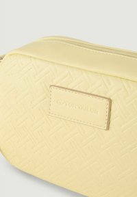 Žlutá syntetická crossbody taška s texturovaným tkaným vzorem, s označením značky a zipem nahoře.