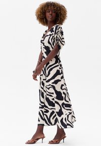 Zwart en crèmekleurig zebraprintjurk met een V-halslijn, korte puffmouwen en een vloeiende silhouet; gecombineerd met open teen bruine hakken.