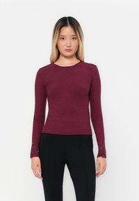 Haut à manches longues côtelé bordeaux avec un col rond et des accents boutonnés aux poignets, fabriqué dans un matériau extensible ajusté pour un fit près du corps.