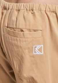 Beige shorts med elastisk midje, med en baklomme og en hvit brodert logo. Laget av lettvektig, teksturert stoff.