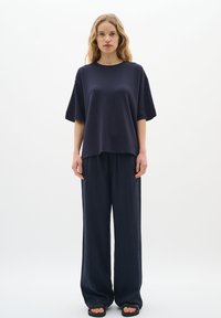 Tengerészkék, nagy méretű, rövid ujjú póló, laza fazonú tengerészkék nadrággal párosítva. Simább szövettextúra, egyszerű dizájn és minimalista stílus.