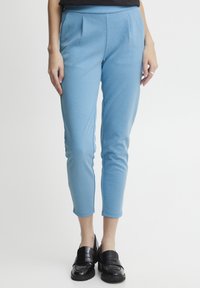 Pantalon ajusté bleu avec des plis à l'avant, fabriqué en un tissu doux et texturé. Longueur courte, associé à des mocassins noirs brillants.