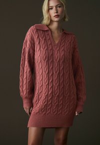 Kabelstickad klänning i dammros, med V-ringning, oversize-krage och ribbade ärmslut och fåll. Mjuk textur med intrikata mönster.