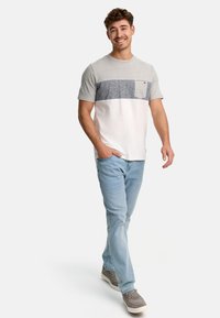 Grå og hvid farveblokeret t-shirt med korte ærmer, udstyret med en blå lommefirkant, båret med lyseblå jeans og grå sko.