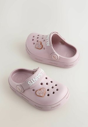 Roza gumijasti klompi z zračnimi luknjami, belim trakom z napisom "ALLSAINTS" in rjavim srčkastim poudarkom na strani.