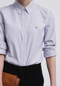 Skjorta med knappfront i små, ljusblå och vita ränder. Tillverkad av bomull, med uppvikta ärmar och en logotyp ovanför vänster bröstficka.
