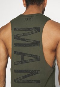 Olive green sleeveless tank top with a large black graphic print on the back, featuring a textured, cut-out design and branded logo.