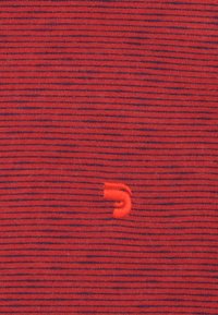 Rood en marine gestreepte stof met een klein, geborduurd oranje logo detail. De gebreide textuur is zichtbaar over het oppervlak.