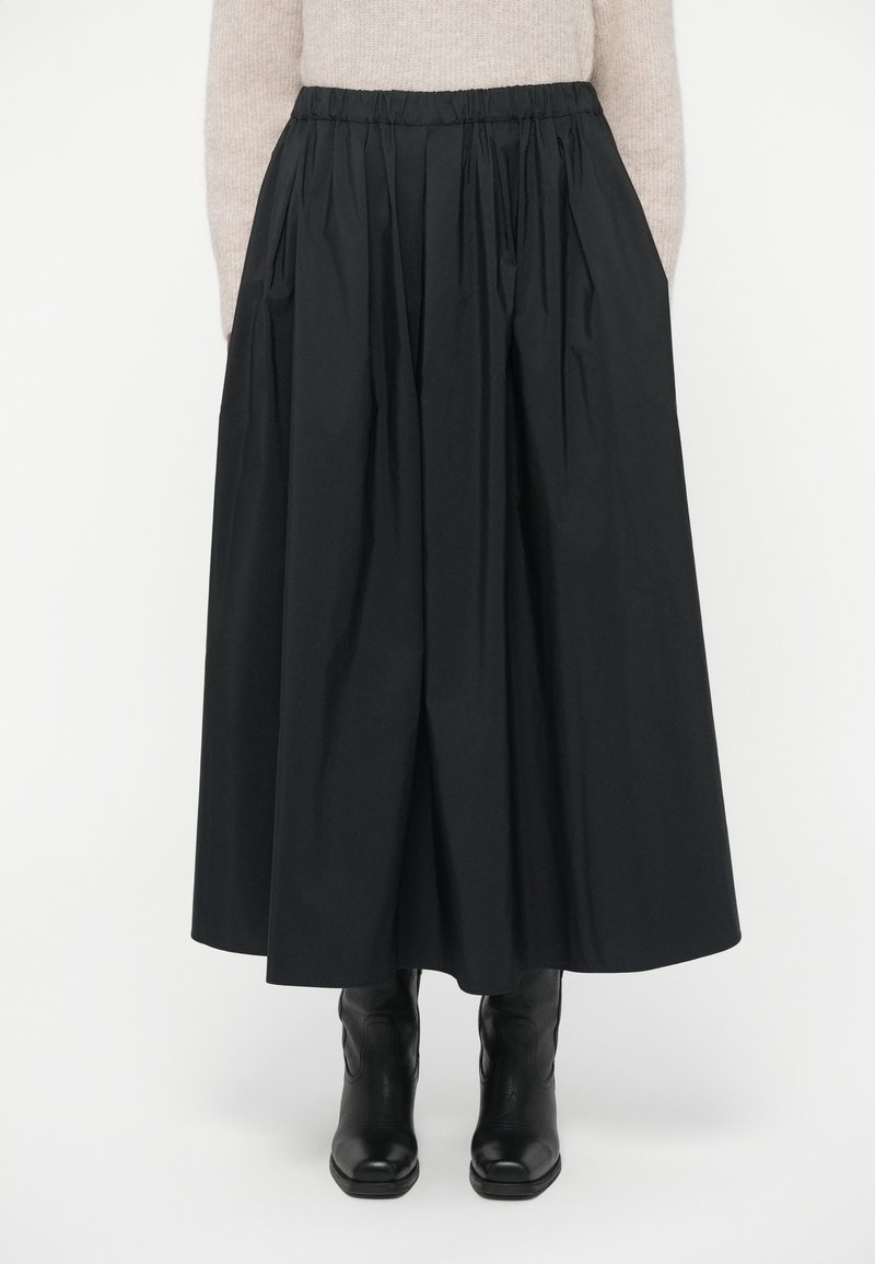 Sort, lang nederdel lavet af letvægtsstof med en samlet elastisk talje og sidelommer, parret med knælange sorte støvler.