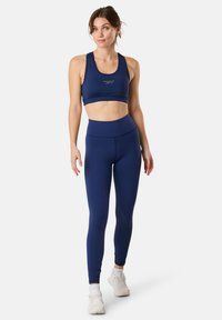 Marinblå sportbh och högmidjade leggings, tillverkade av ett slätt, elastiskt tyg med minimala designdetaljer. Vita sneakers fulländar stilen.