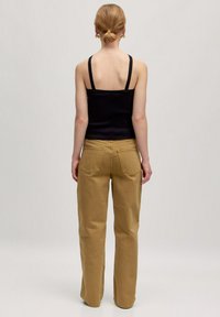 Zwarte geribbelde tanktop met dunne banden, gecombineerd met loszittende kaki broek met achterzakken, gezien van achteren.
