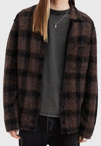 Brun och svart rutig button-up skjorta i mjukt material; har en bröstficka, stora knappar och avslappnad passform. Bärs över en grå skjorta.