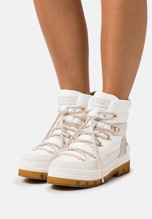Stivaletti bianchi alla caviglia in pelleTexture e suede, con spesse stringhe beige, logo sul colletto imbottito e una suola in gomma resistente.