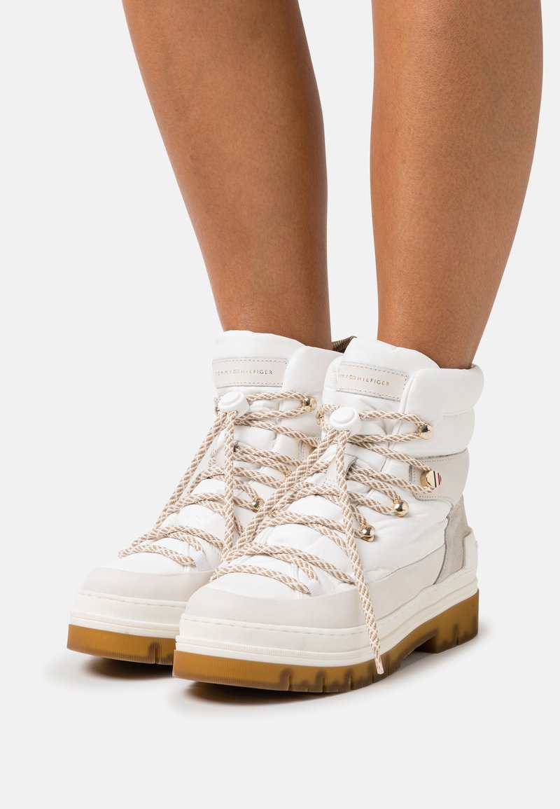 Stivaletti bianchi alla caviglia in pelleTexture e suede, con spesse stringhe beige, logo sul colletto imbottito e una suola in gomma resistente.