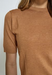 Hnědý krátký rukáv pletený top s kulatým výstřihem. Látka má jemnou strukturu a elastický materiál, s přiléhavými rukávy a tělem.