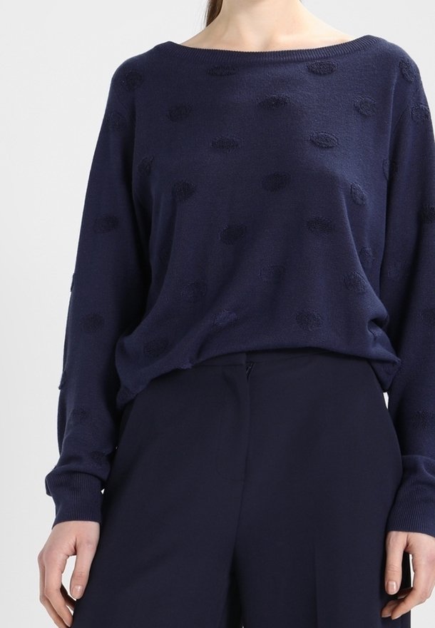 Femme portant un pull bleu marine à manches longues avec des pois texturés et un pantalon taille haute bleu marine assorti.