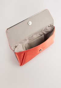 Pochette en tissu pêche avec une fermeture métallique, dotée d'un intérieur beige et d'une poche. Texture lisse, forme carrée et design simple.
