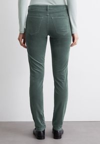 Groene, fitted broek gemaakt van een zachte stof. Opmerkelijke details zijn onder andere twee achterzakken en een gladde tailleband, getoond vanuit de achterkant.