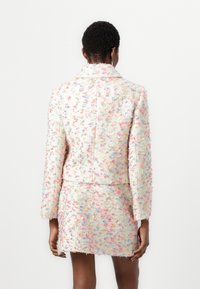 Strukturierte Tweedjacke mit mehrfarbigen Einsprengseln, Reverskragen und passendem Minirock. Merkmale sind lange Ärmel und taillierter Schnitt.