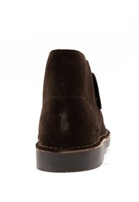 Bottine en daim marron avec un bout rond, une texture lisse et des coutures contrastées. Dotée d'une semelle en caoutchouc robuste et sans éléments métalliques visibles.