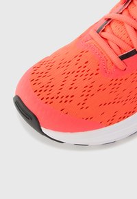 Baskets de sport corail vif avec une tige en mesh texturé, un motif unique, des lacets fins et une semelle extérieure noire.