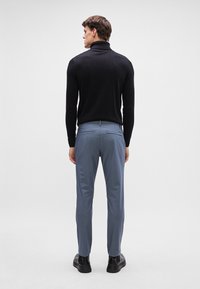 Schwarzer Rollkragenpullover und hellblaue Hose aus glattem Stoff, taillierte Passform und schlichtes Design. Schwarze Schuhe runden das Outfit ab.