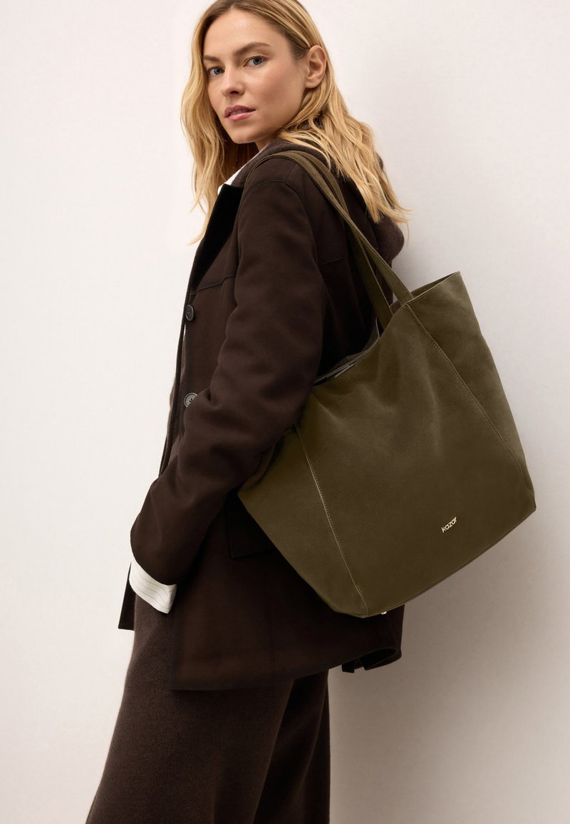 Olíva zöld vászontáska sima felülettel és két erős füllel. Diszkrét márkajelzés a fronton, semleges háttérrel.