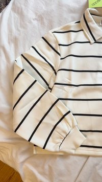 Polo a maniche lunghe bianco con strisce orizzontali nere, colletto a risvolto e polsini a costine. Materiale morbido con vestibilità rilassata.
