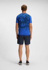 Blå athletic t-shirt med et pixeliseret sort mønster på ryggen, parret med mørke shorts og sorte sneakers. Glat stof og enkelt design.