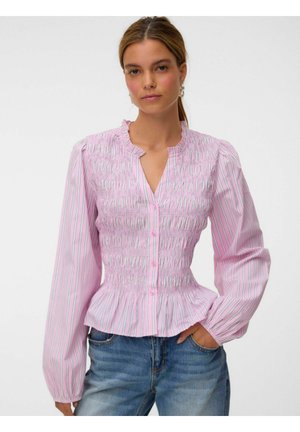 Femme portant un chemisier rayé rose et blanc boutonné, avec un corsage smocké et des manches longues, associé à un jean bleu en denim.