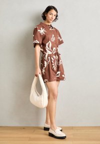 Vestito marrone a maniche corte con motivi a foglia bianchi, vita cincherata, abbinato a una borsa beige e scarpe con plateau di colore chiaro.